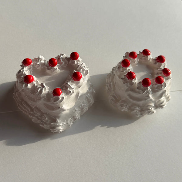 Two small cakes with white frosting and red cherries on a light gray background