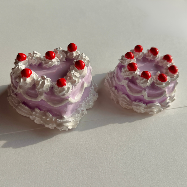 Two miniature purple cakes with white frosting and red berries on a light gray background